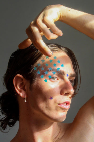 Boy holding a sheet of cute star pimple patches and wearing holographic starface Australia